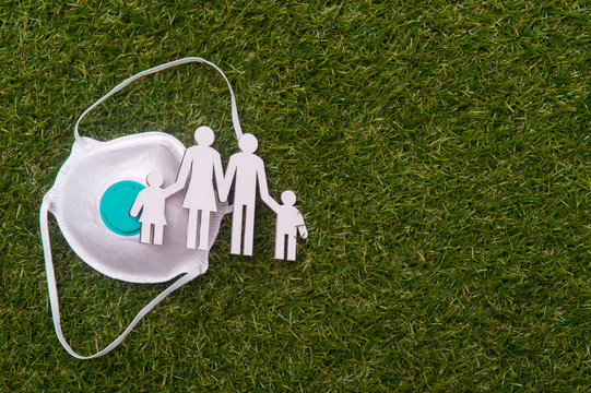 Cardboard figures of the family  and mask on green grass background. Coronavirus or Covid-19 virus concept