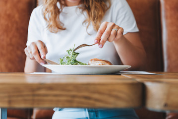 Young caucasian woman with curly hair in white t-shirt eating salad and chicken in a restaurant