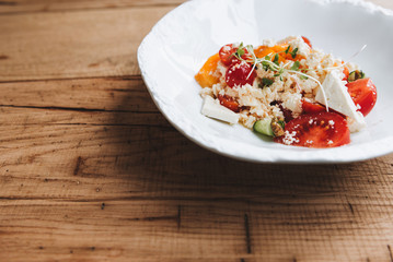Feta cheese and tomato salad with green peas sprouts on a simple white plate on a rough wooden surface 