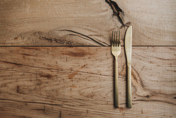 Golden colored stainless steel cutlery set of knife and fork on an authentic rough wooden table surface with space for text