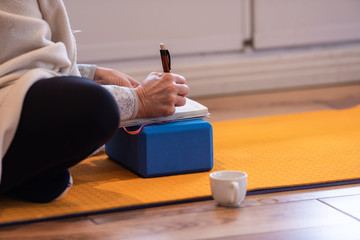 Side view of elderly woman writing notes during the workshop in the yoga center. Medium shot of female making notes. Beginner studying yoga