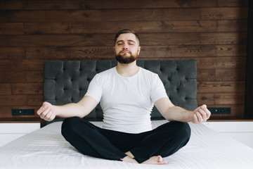Fototapeta premium Handsome caucasian man meditating and practicing mindfulness on his bed in bedroom