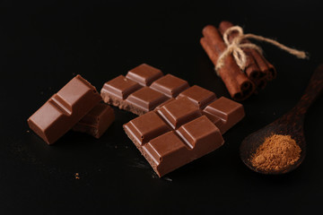Chocolate with cinnamon on a dark background, with cinnamon sticks in the background