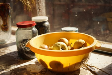 Natural yellow apples in a yellow bowl on a sunny rustic windowsill