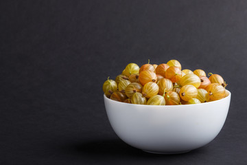 Fresh green gooseberry in white bowl on black background. side view.