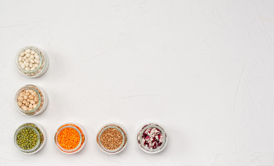 A variety of dry cereals for vegetarians in glass jars: lentils, chickpeas, beans, buckwheat on a white background. Copy space