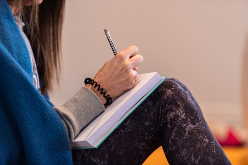 Close-up view of female hands making notes in the yoga class. Unrecognizable woman studying secrets of yoga poses. Side view