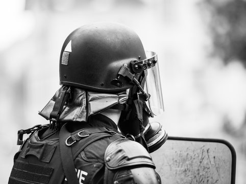 Black and white image of police officer wearing gas mask against tear gas at protest with Yellow jackets Gilets Jaunes