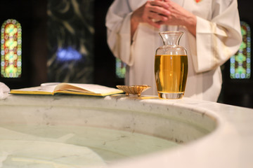  Priest in front of a baptismal font with a bible. Baptism scene. Priest praying in a church. Open...