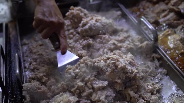 Vendor spreading meat guts with spatula across the griddle in preparation for tacos