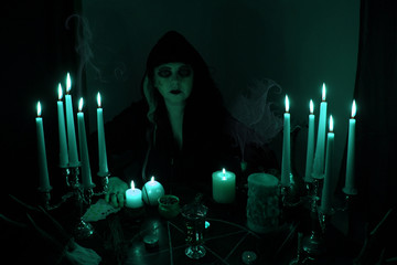 Female Fortuneteller conjures in a dark room, candles are burning on a round esoteric table with a...