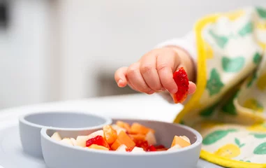 Macro Close up of Baby Hand with a Piece of Fruits Sitting in Child's Chair Kid Eating Healthy Food