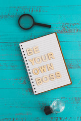 being a business owner, notebook on desk with Be your own boss text surrounded by lightbulbs symbol of good ideas