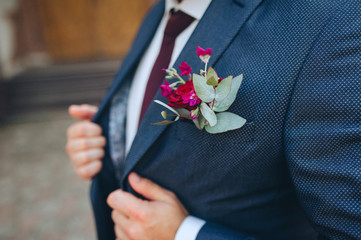Closeup of groom's boutonniere and blue suit. Flowers of rose, white shirt and burgundy tie.