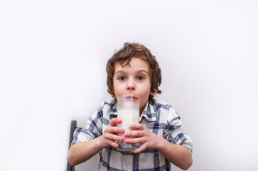Curly boy drinks milk. joyful boy with a glass of milk on white background. Source of calcium. Concept of lactose deficiency