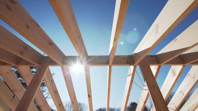 Sliding view from below of roof beams and the sun shining through them. Frame house under construction
