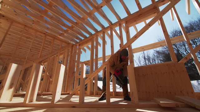 Worker is nailing wooden planks inside the frame house under construction