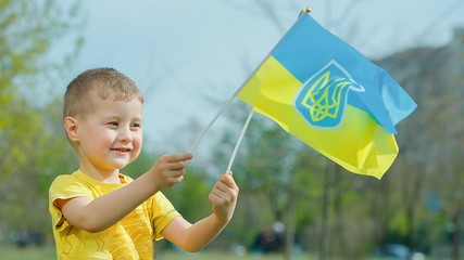 flag of Ukraine is blue-yellow fluttering in wind against sky in hands of little Ukrainian boy in yellow T-shirt. Happy child celebrates Ukraine's Independence Day and Flag Day