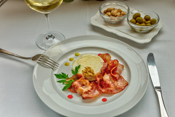 Warm goat cheese with honey and bacon served on a white dish, served with a glass of delicate white wine