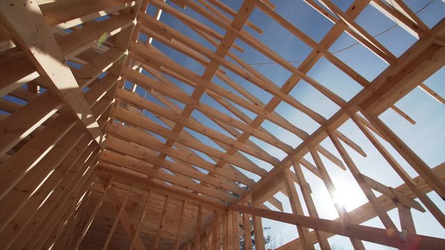 View from below of the wooden roof planks against bright blue sky. Frame house under construction