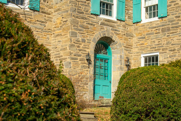 A Teal Door on an old Cobblestone House With Two Bushes in the Foreground