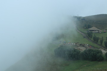 Fototapeta na wymiar The fog is coming in from the edge of a cliff in de andes near quito, slowly covering the horse stable, path and house
