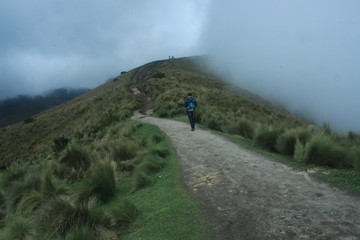 Obraz premium A lone hiker walking over a path in the Andes while fog is slowly covering the whole track