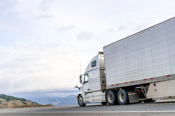 White big rig semi truck transporting food in refrigerator semi trailer driving on the road with sky and hills view