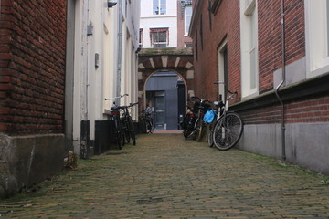 Small alley looking old, paved with pebbles and surrounded by brick walls with bicycles parked at both sides