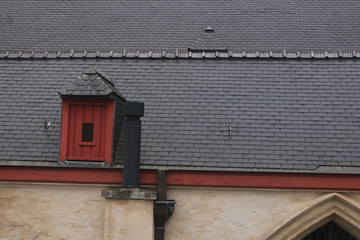 Well laid roof covered in small black tiles, with a very small red window and a new black metal chimney