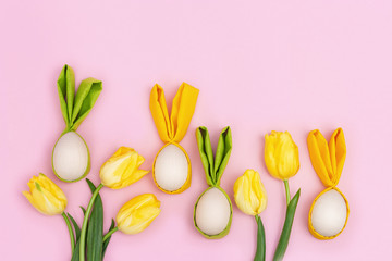 Easter composition with handmade colorful easter eggs with ears from rabbit and bouquet of fresh yellow flowers tulip on pink background with copy space. View from above, flat lay.