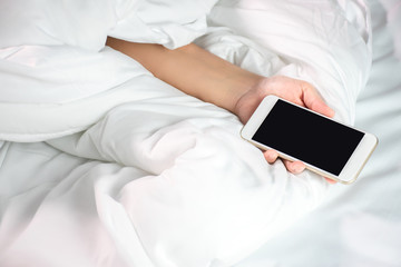 A woman lying in bed and holding a smartphone