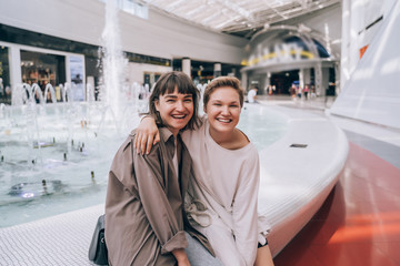 Two girls have fun in the mall, a fountain in the background