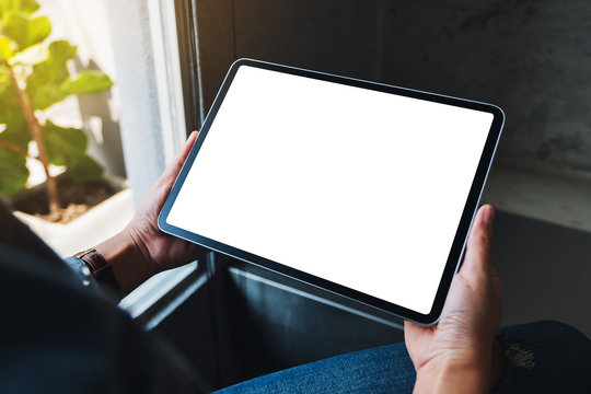 Mockup image of a woman holding black tablet pc with blank white horizontal screen in cafe