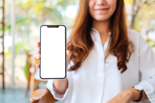 Mockup image of a beautiful woman holding and showing mobile phone with blank white screen in cafe