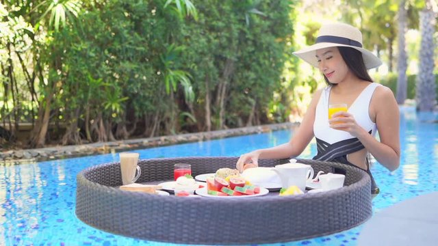 A young woman holding a glass of orange juice in one hand spins the floating food platter looking for just the right breakfast food. 