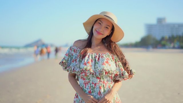 Close-up narrow depth of field, Pretty young Asian woman in a bohemian flower dress stands on the beach smiling enjoying the ocean breeze.
