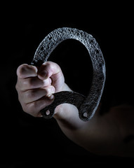 A man holds an old, rusty horseshoe against a black background in his hand. Concept: talisman and...