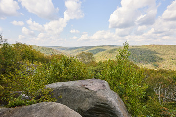 The Minister Creek Trail overlook in Allegheny National Park. In the distance can be seen the hills, mountains, valleys, and forests of the park. In the foreground is a large stone boulder.
