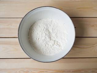 Wheat white flour in a metal cup on a wooden surface. Ingredient for Russian pancakes