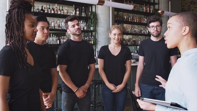Female restaurant bar manager with digital tablet giving motivational talk to waiting staff before opening - shot in slow motion