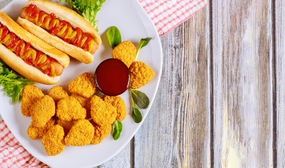 Breaded chicken nuggets and hot dog with mustard on white plate.