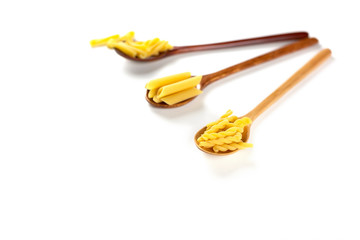 Various types of italian pasta concept. Raw gemelli, penne, casarecce in wooden spoons on white background. Copy space.