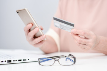 Senior woman checks her finance on credit card with smartphone