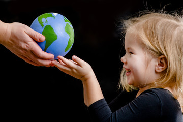 Mother gives the planet into the hands of a child. Isolated on dark background