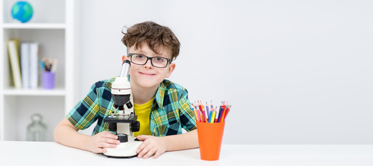 Smiling smart boy sits with microscope at home. Empty space for text