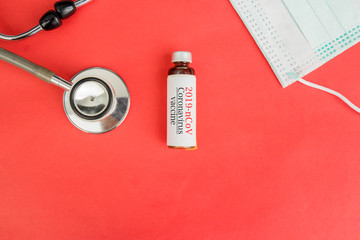 medical stethoscope, health mask and coronavirus vaccine bottle isolated over red background