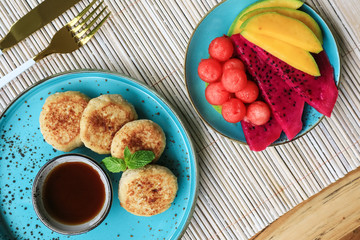 Vegan tofu cheese pancakes on blue plate with fresh tropical fruits and coconut cream, top view