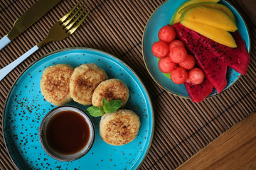 Vegan tofu cheese pancakes on blue plate with fresh tropical fruits and coconut cream, top view
