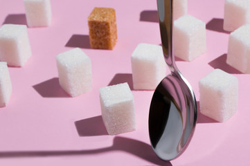 square pieces of cane sugar and a metal spoon on a pink background